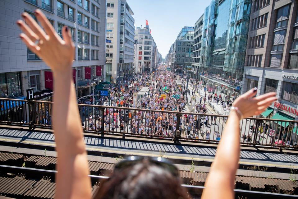 Eine junge Frau winkt der Menschenmenge zu, die bei der Demonstration gegen Corona-Maßnahmen über die Friedrichstraße zieht.<span class="copyright">Christoph Soeder / dpa</span>