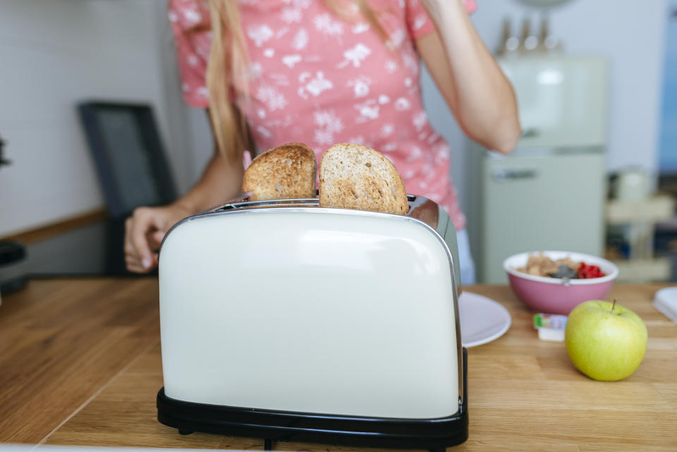 Getoastetes Brot im Toaster, Frau steht am Tisch dahinter