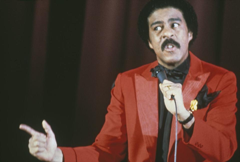 richard pryor talking on stage into a microphone while wearing a red suit