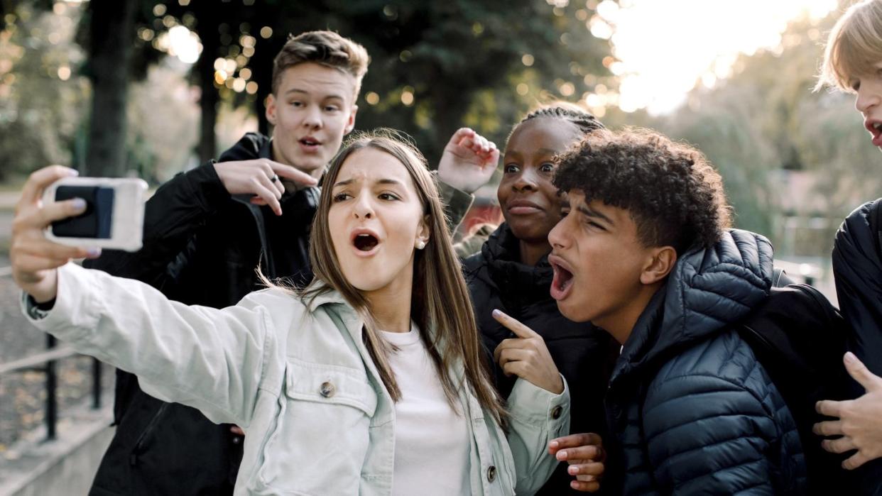 cheerful teenage friends taking selfie through mobile phone while standing on street in city