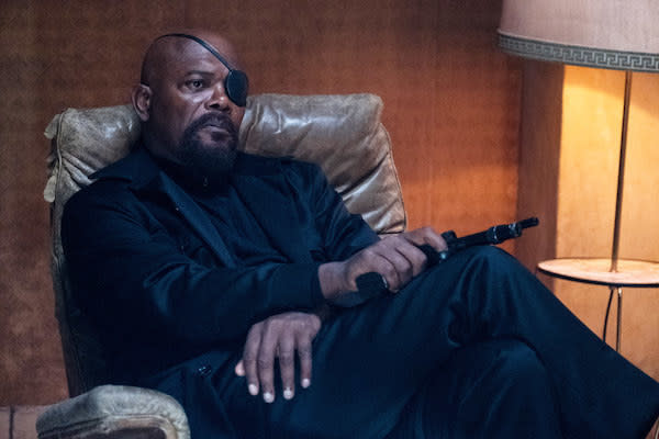 Samuel L. Jackson holds a gun while sitting down in a chair