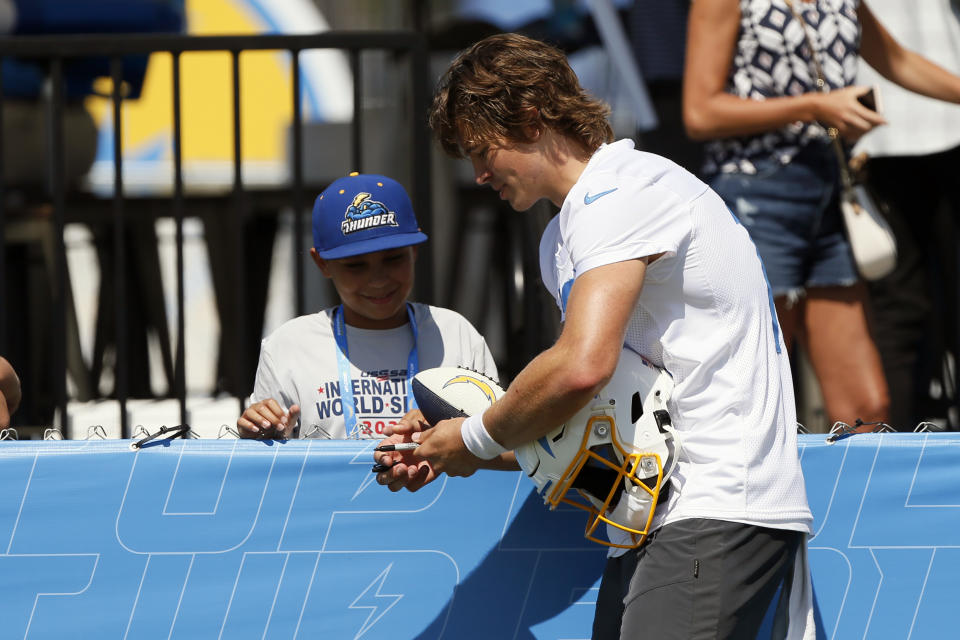 Los Angeles Chargers quarterback Justin Herbert, right, signs an autograph for a fan after practice at the NFL football team's training camp in Costa Mesa, Calif., Wednesday, July 28, 2021. (AP Photo/Alex Gallardo)