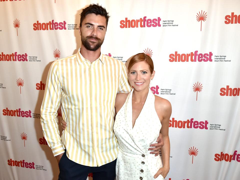 tyler stanaland and brittany snow on a casual red carpet in 2018. he has his arm around her waist, and they're both smiling