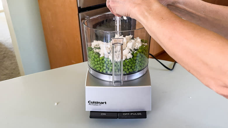 Adding fresh goat cheese to cooked peas in food processor bowl