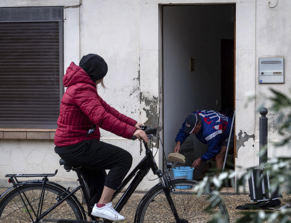 A woman rides past a man cleaning his house in the town of Villegailhenc, southern France, Monday, Oct.15, 2018. Flash floods tore through towns in southwest France, turning streams into raging torrents that authorities said killed several people and seriously injured at least five others. (AP Photo/Fred Lancelot)
