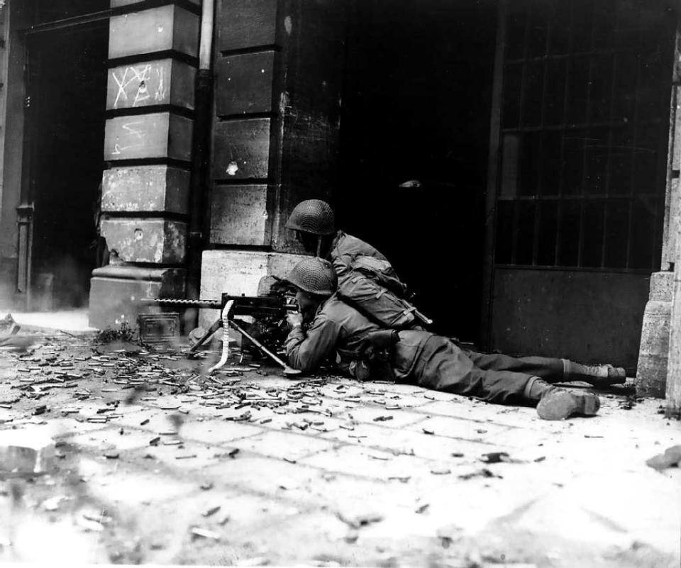 US-amerikanische Soldaten liegen mit einem Maschinengewehr während des Zweiten Weltkrieges in den Straßen von Aachen in Deckung. (Bild: ddp)