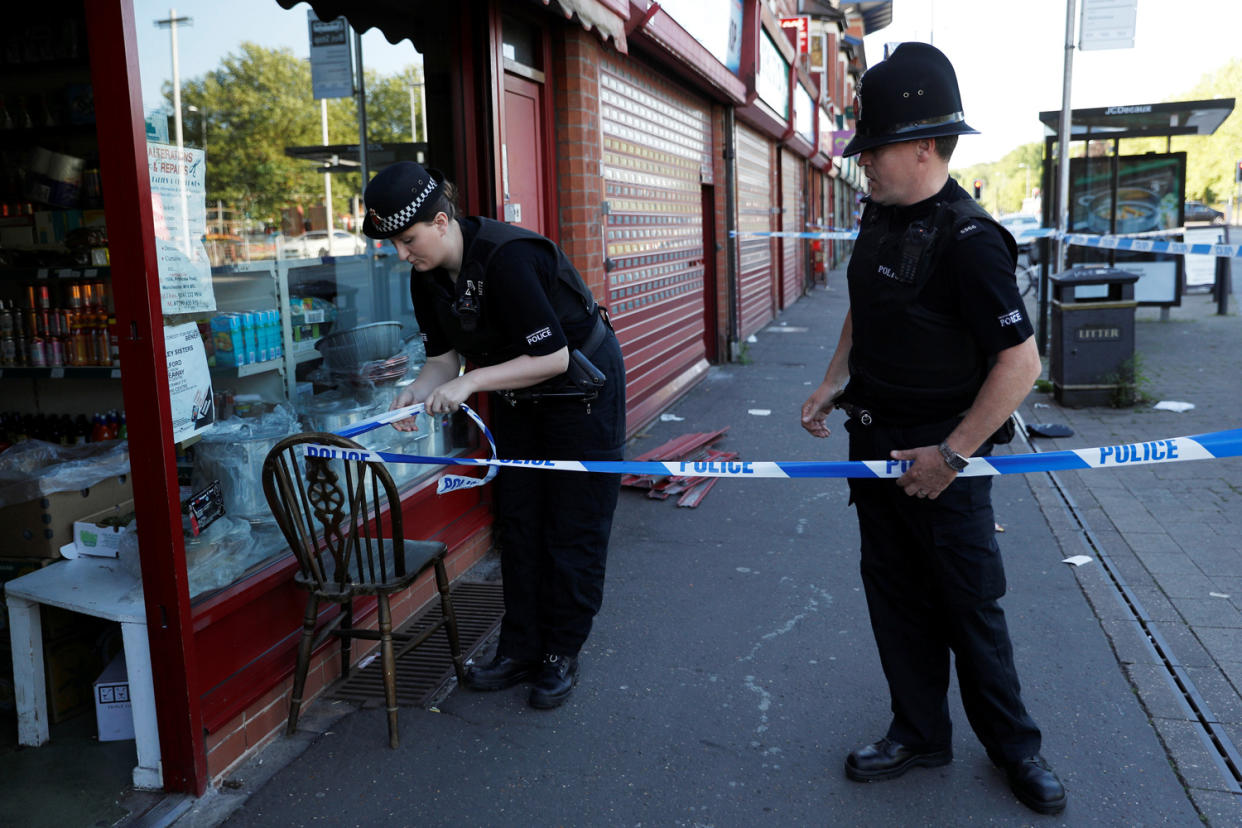 Police officers tie up cordon tape outside a barber's shop in Moss Side after a raid: Reuters