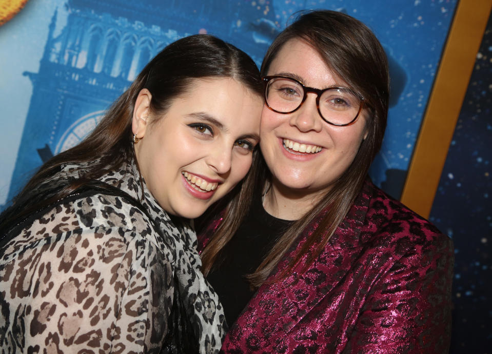 Beanie Feldstein and Bonnie Chance Roberts smile together at an event, Beanie in a leopard print top and Bonnie wearing glasses and a sparkly jacket