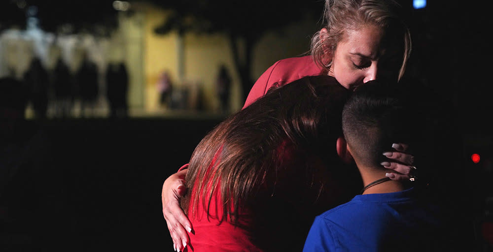 Three people are outside at night, hugging