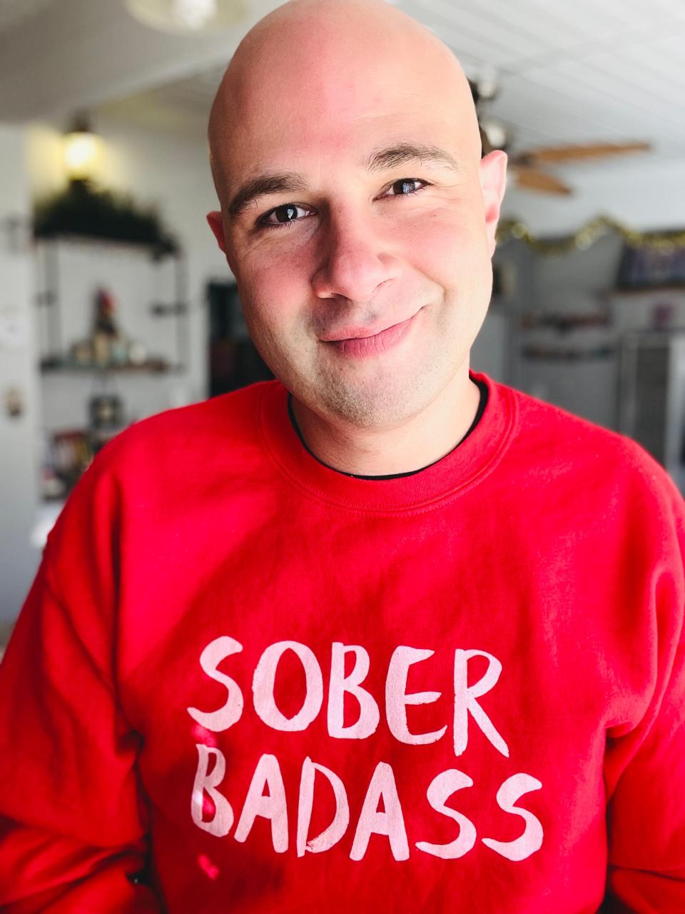 Anthony Eder smiles in a selfie with a red sweatshirt reading "sober badass."