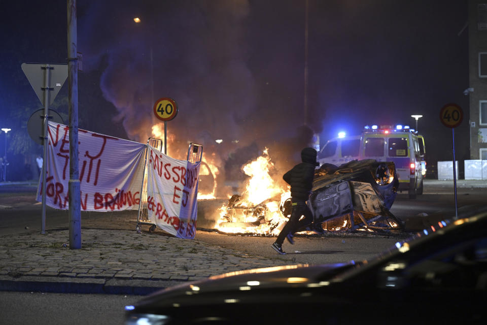 FILE - A person runs past a burning car and a banner reading, "No to Quran burning. Don't abuse freedom of expression" placed on the roundabout, at Ramel väg, in Malmo, Sweden, early Monday Sept. 4, 2023. The targeting of Swedish citizens in an attack in Brussels on the night of Monday, Oct. 16, 2023 has shocked the Scandinavian country, yet the government had been warning for months that Swedes were at greater risk since a recent string of public desecrations of the Quran, Islam's holy book, by a handful of anti-Islam activists. (Johan Nilsson /TT News Agency via AP, File)