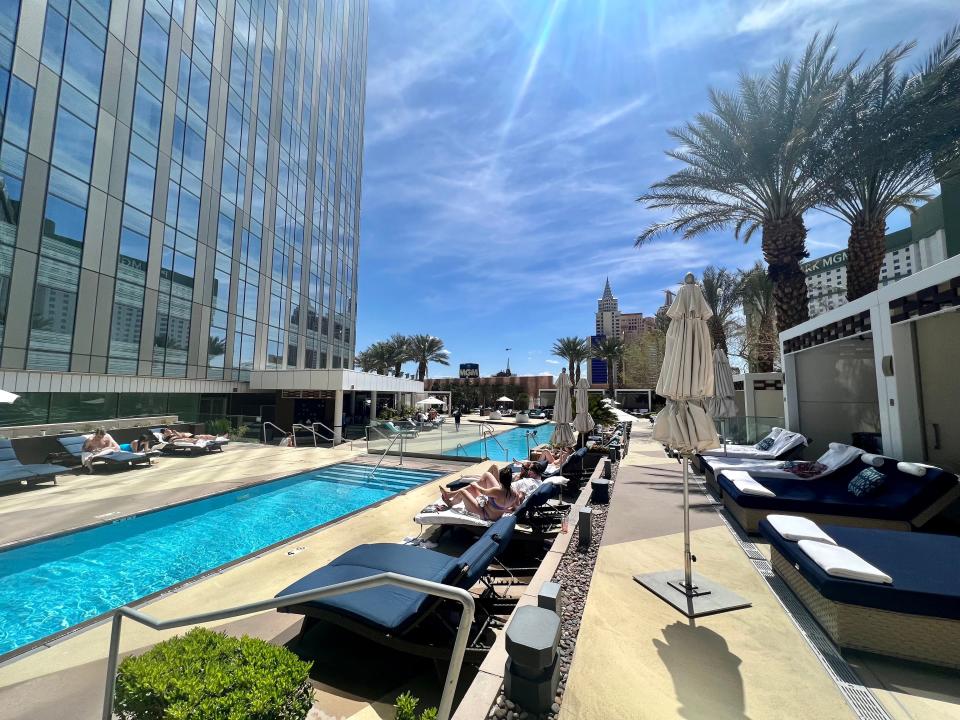 Two pools next to a skyscraper on one side and loungers with people around the pool.