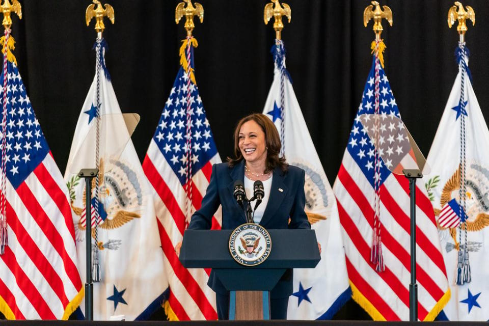 Vice President Kamala Harris standing at a podium in front of flags.