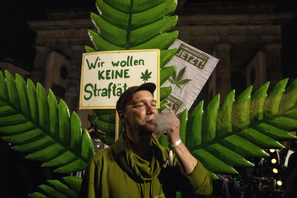 A man takes a puff from a marijuana cigarette in front of the Brandenburg Gate and a placard reading "We don't want to be offenders!" during the 'Smoke-In' event in Berlin, Germany, Monday, April 1, 2024. Starting 1 April, Germany has legalised cannabis for personal use. As per the new law, Adults aged 18 and over will be allowed to carry up to 25 grams of cannabis for their own consumption. (AP Photo/Ebrahim Noroozi)