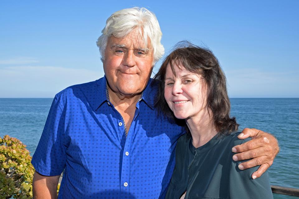 Jay Leno in a royal blue button down wraps his arm around wife Mavis in a dark teal shirt