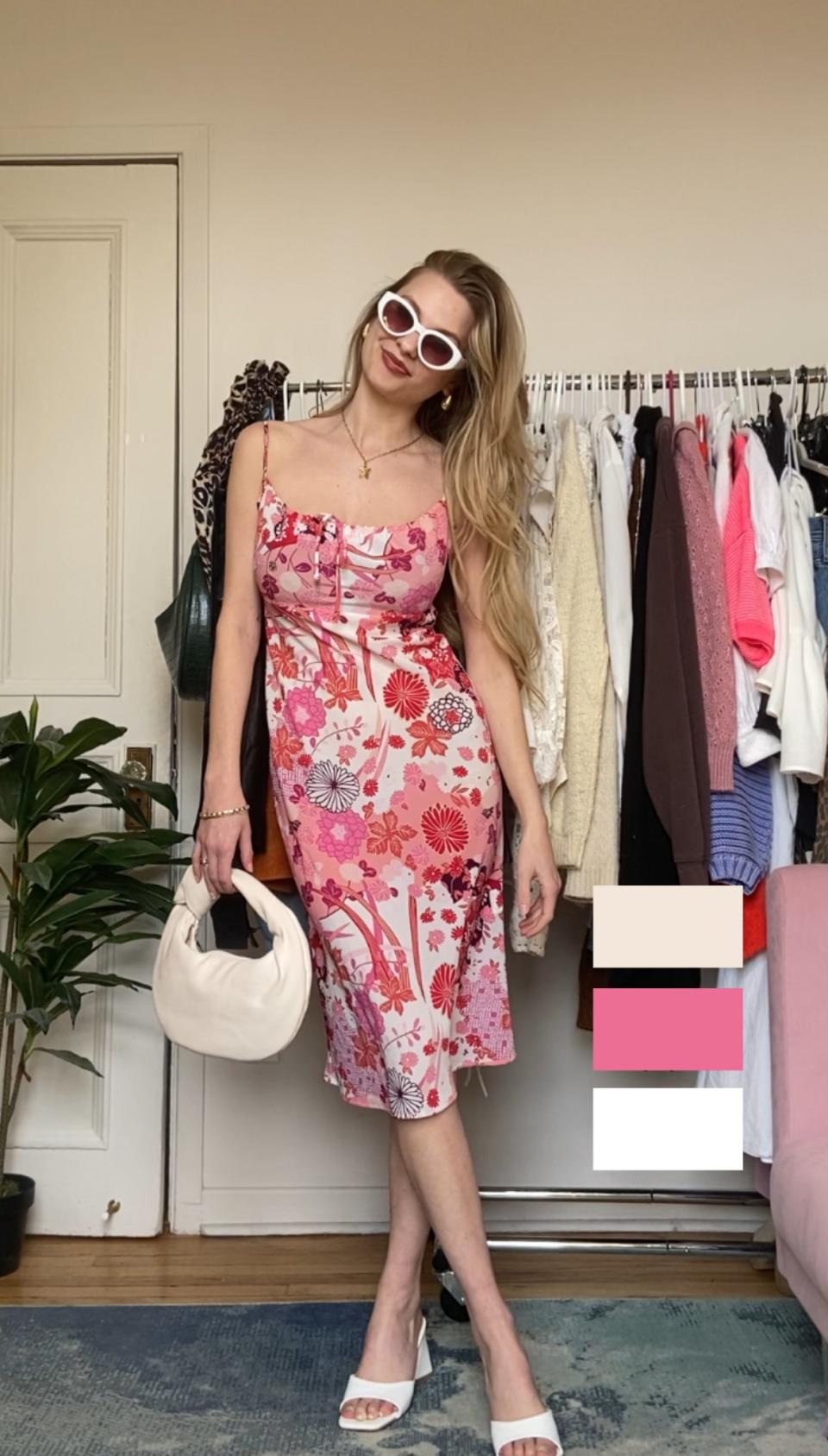 Woman in patterned dress with handbag and sunglasses standing in a room with clothes rack behind