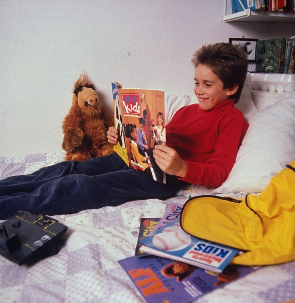 Boy on bed reading a magazine; plush toy beside him; retro vibe