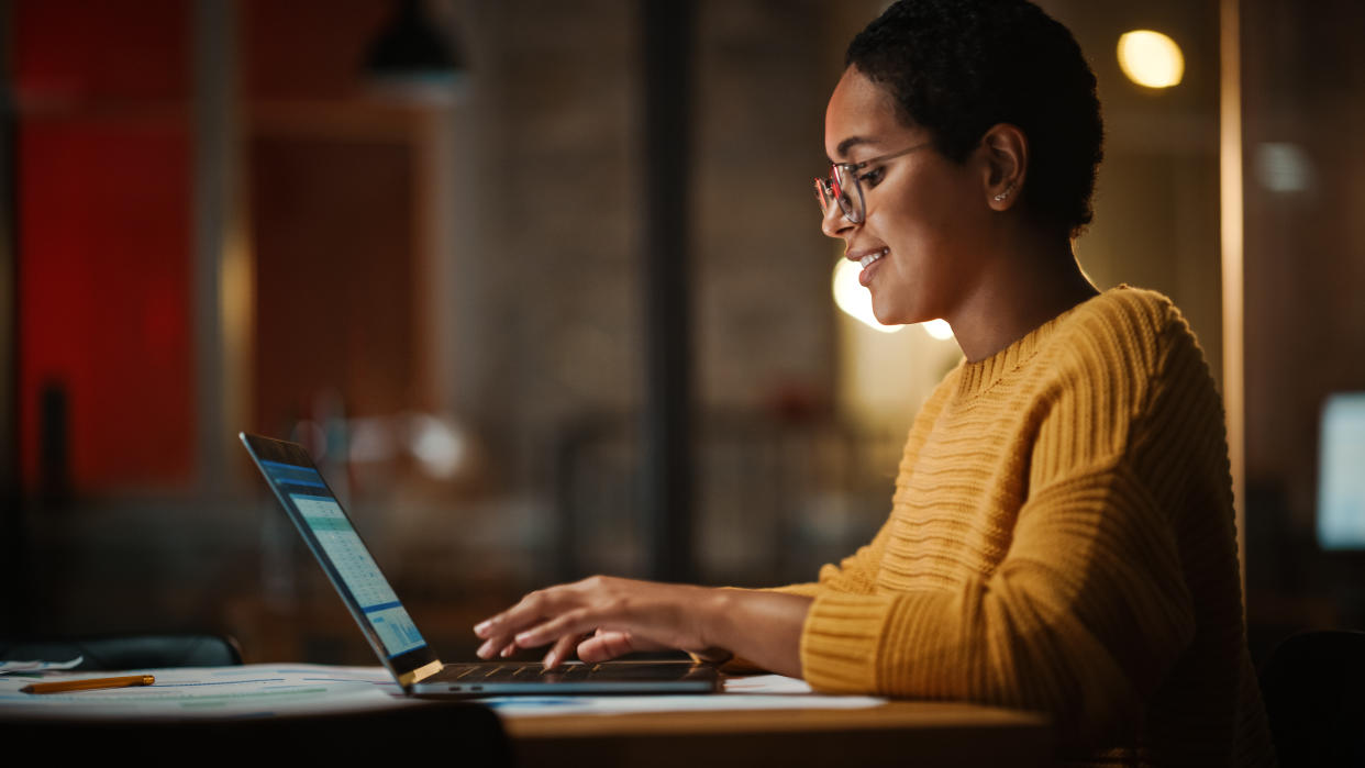  Woman seated at a table working on a laptop in the evening. 