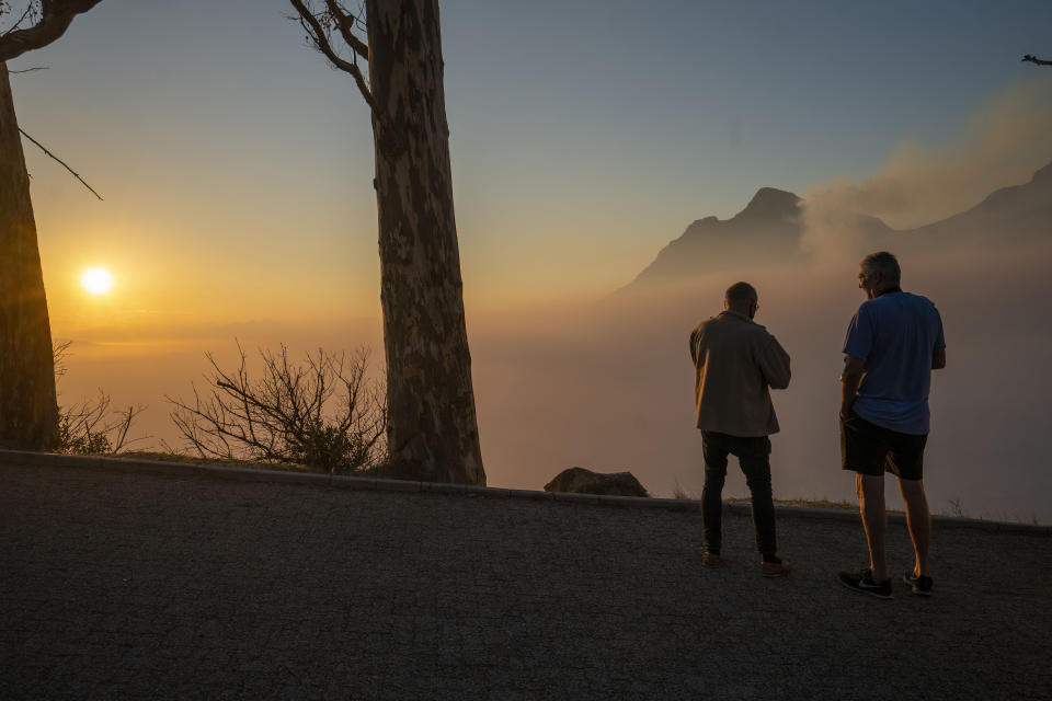 Capetonians watch the sun rise from the top of Signal Hill as smoke engulfs the city of Cape Town, South Africa, Tuesday, April 20, 2021. A massive fire spreading on the slopes of the city's famed Table Mountain, at right, is kept under control as firemen and helicopters take advantage of the low winds to contain the blaze. (AP Photo/Jerome Delay)