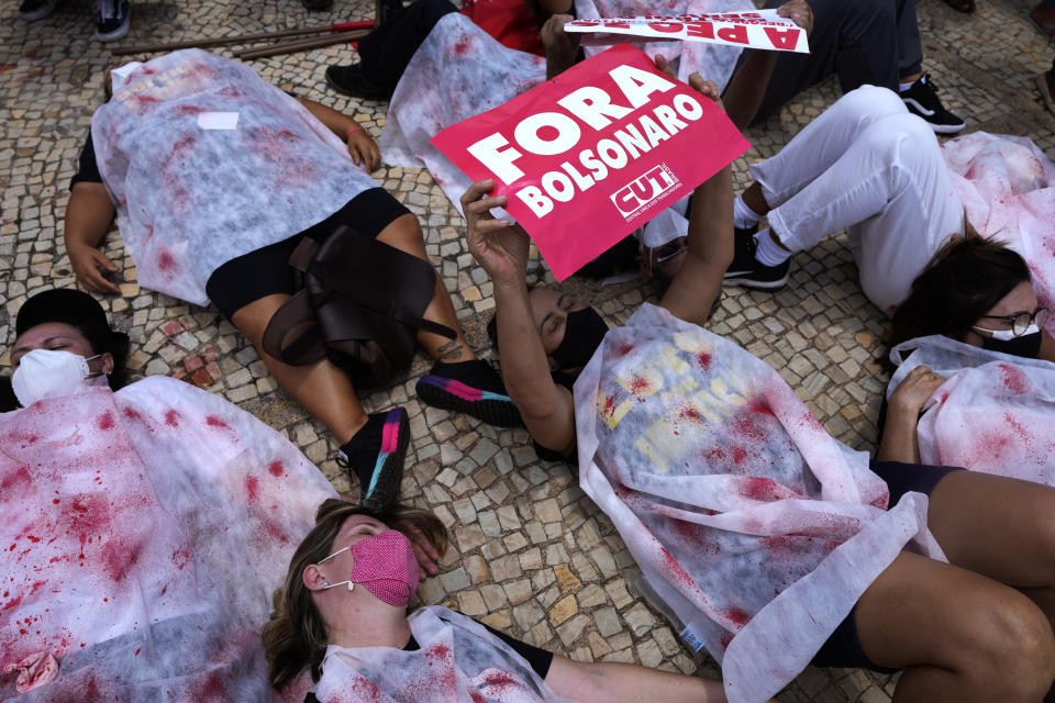 Demonstrators are dressed in sheets covered by fake blood to represent people who died of COVID-19, one holding the Portuguese message "Get out Bolsonaro," referring to the president, outside the Planalto presidential palace, in Brasilia, Brazil, Wednesday, Oct. 20, 2021. (AP Photo/Eraldo Peres)