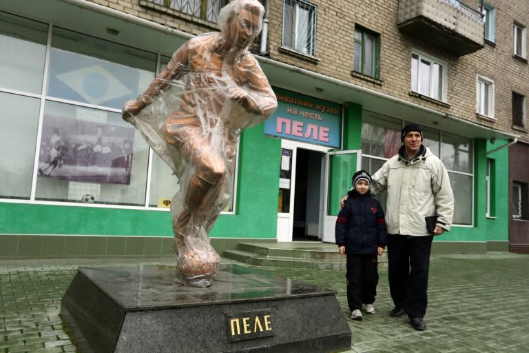 A man poses with his child next to the Pele sculpture outside the museum dedicated to the retired Brazilian football player in the eastern Ukrainian city of Lugansk