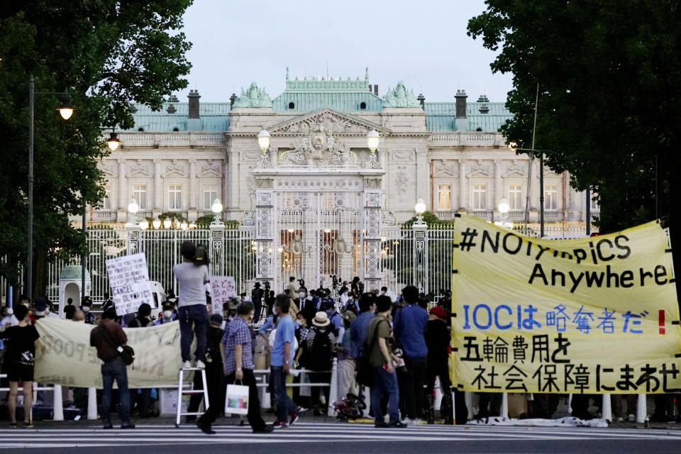 Protesters against the Tokyo Olympics gather outside Akasaka Palace, Japanese state guest house where the welcome party for IOC President Thomas Bach and its officials are held in Tokyo, Japan, Sunday, July 18, 2021. The banner, yellow, reads "IOC is a looter ! Use Olympic fees for social welfare". (Koji Harada/Kyodo News via AP)