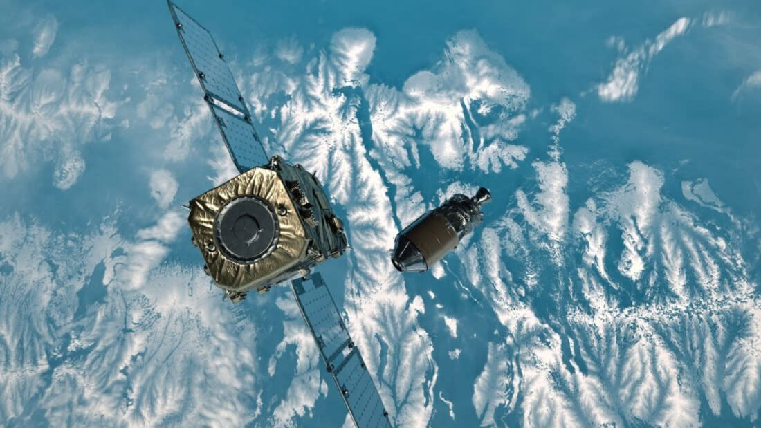  A cube shaped satellite moves toward a spacecraft hovering above some snowy mountains on earth. 