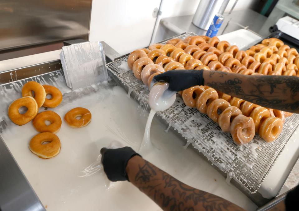LaTisha Shaw, 48, of Detroit, transfers doughnuts coated in glaze to a tray at Dutch Girl Donuts in Detroit on Friday, May 3, 2024.