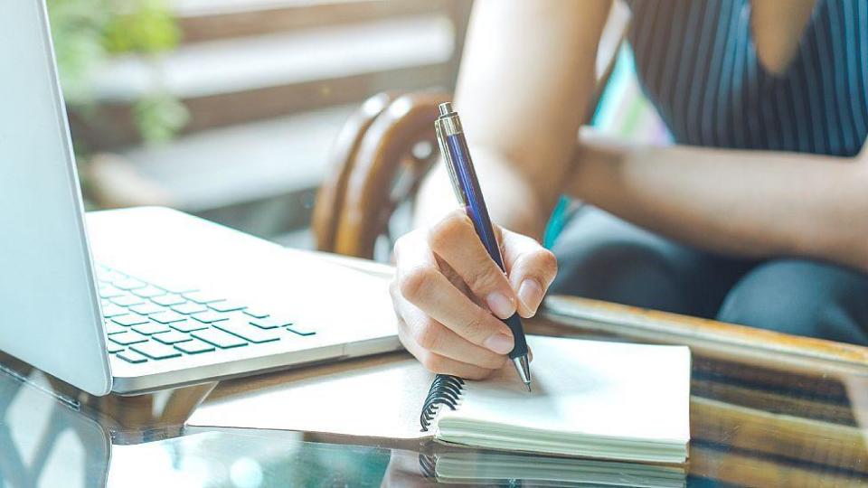 Mujer escribiendo a mano con un laptop al lado