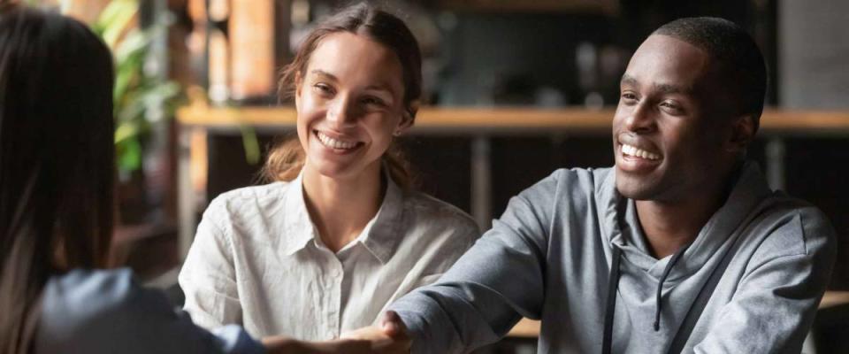 Happy young couple shake hand of woman sitting across the table from them.