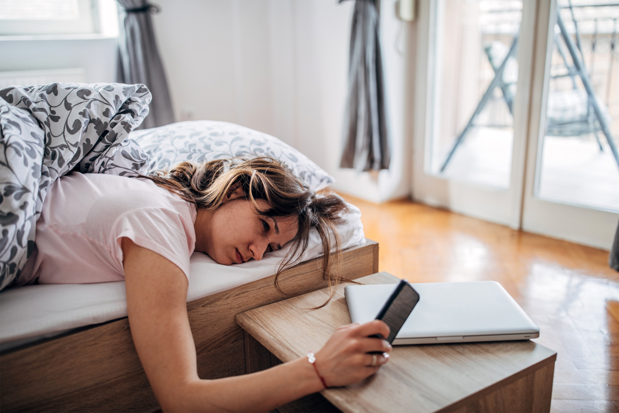 Sleepy woman looking at her phone in bed