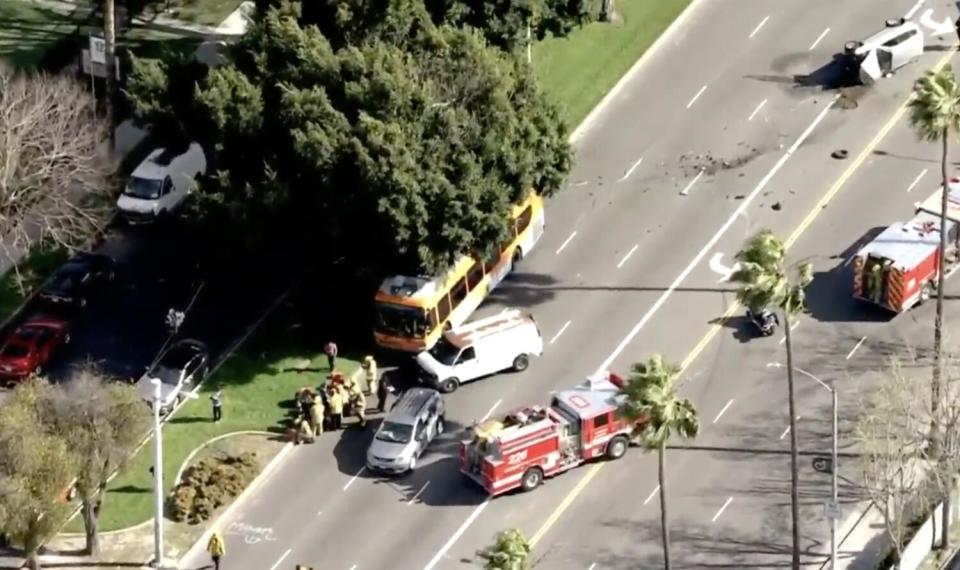 A bus, van, minivan and firetrucks at the scene of a crash where another vehicle rests on its side.