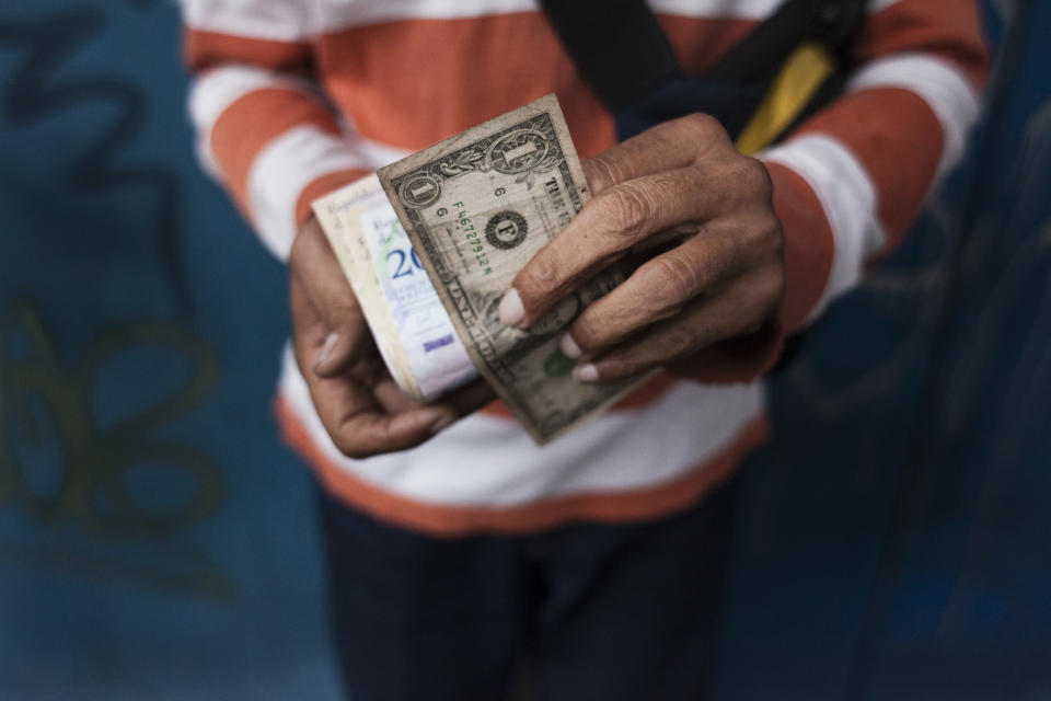 A man holds a U.S. Dollar banknote and a bundle of Venezuelan Bolivar banknotes in Caracas, Venezuela. Photographer: Adriana Loureiro Fernandez/Bloomberg