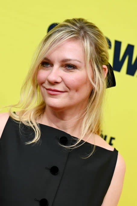 Kirsten Dunst with a bow in her hair, wearing a sleeveless black dress with button details, smiling at a SXSW event