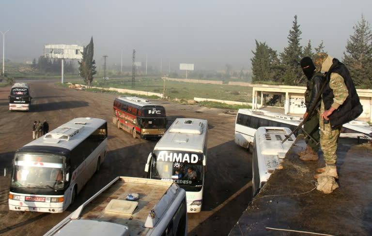 Syrian opposition fighters stand on top of a vehicle in rebel-held Rashidin, west of Aleppo city, as buses carrying people from government-held Fuaa and Kafraya arrive as part of an evacuation deal