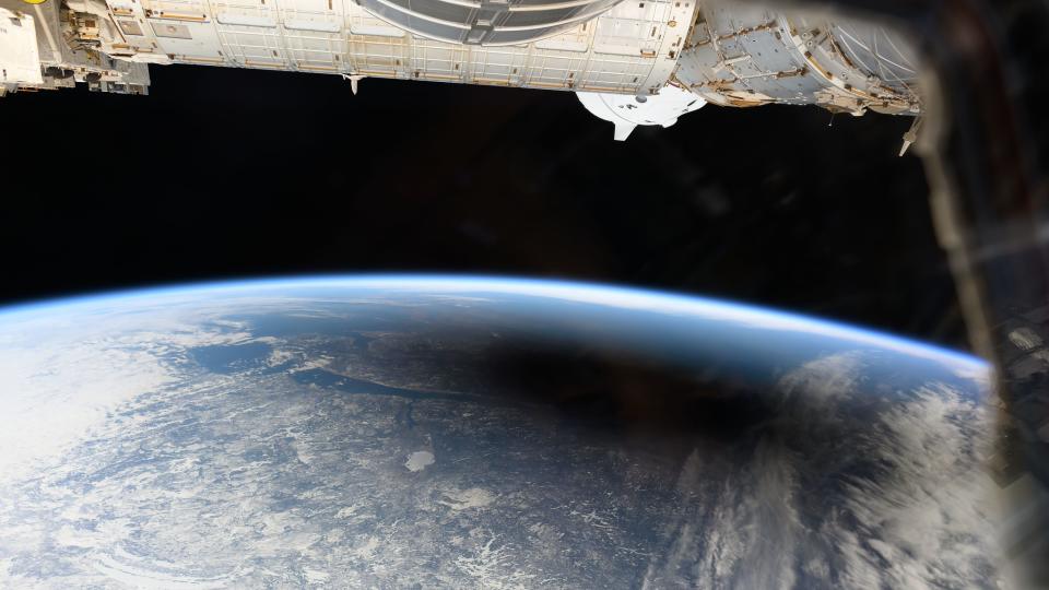 the earth with a black shadow over it.  The modules of the International Space Station are visible just above