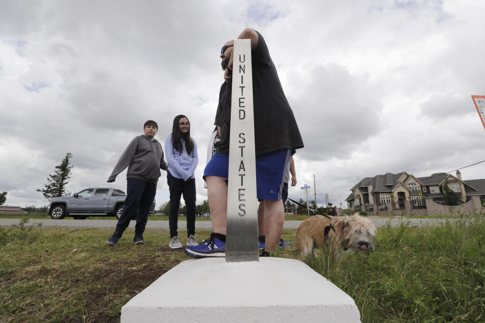 In this photo taken May 17, 2020, Darious Kilgore leans on a marker designating the border with the U.S. as he stands in Canada and visits with family members in the U.S. near Lynden, Wash. With the border closed to nonessential travel amid the global pandemic, families and couples across the continent have found themselves cut off from loved ones on the other side. (AP Photo/Elaine Thompson)