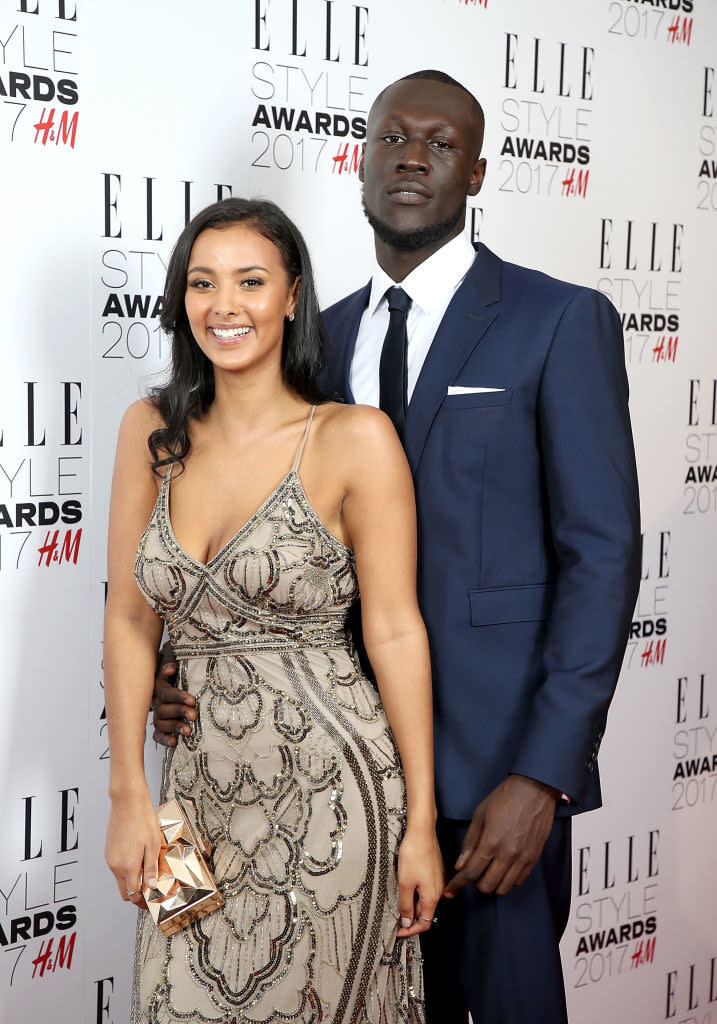 Maya in embellished gown with clutch and Stormzy in suit standing together at an event