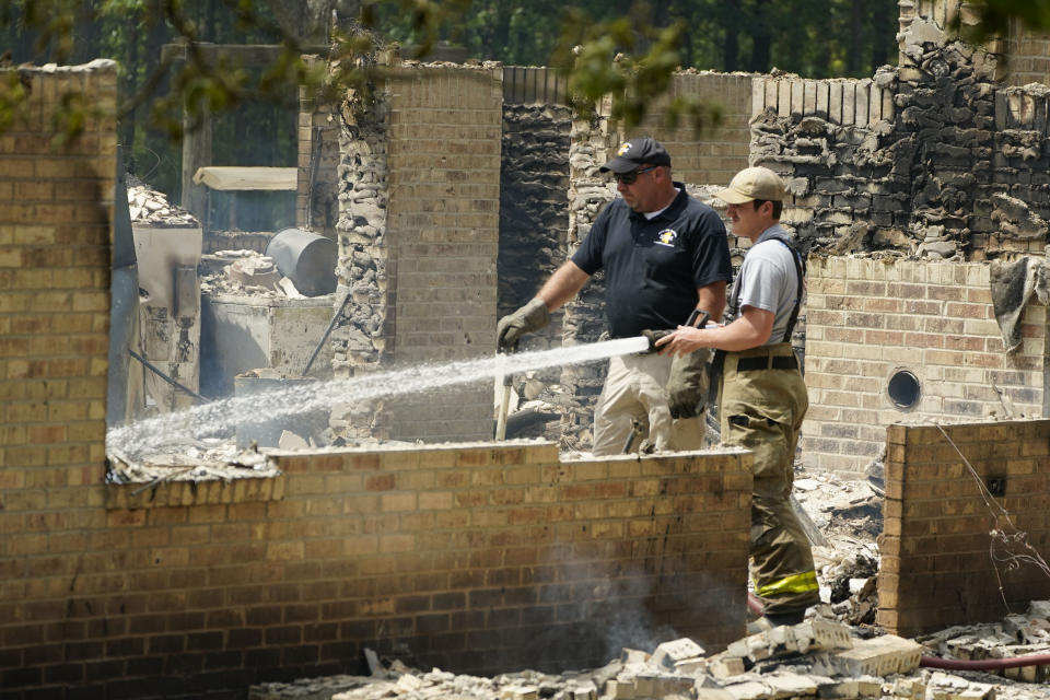 A member of the Mississippi State Fire Marshal's Office, left, waits as a firefighter waters down hot spots inside a burned out house, Wednesday morning, April 26, 2023, in Conway, Miss. Authorities believe a man who escaped from a Mississippi jail over the weekend with three others, and is suspected of killing a pastor, is believed to be dead in the house after a shootout with authorities and barricaded himself inside a burning home near Conway, Mississippi. (AP Photo/Rogelio V. Solis)