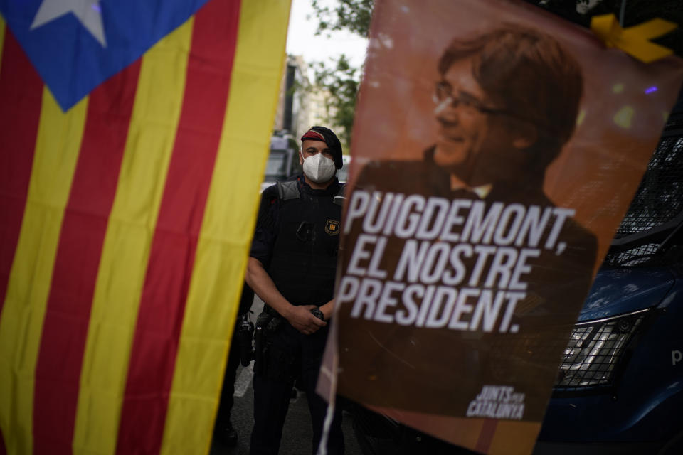 A mossos d'esquadra police officer stands behind a banner and a Catalonia independence flag with the image of former Catalan leader Carles Puigdemont with the message 'Puigdemont , Our leader' as people take part in a protest outside the Italian consulate in support of Puigdemont in Barcelona, Spain, Friday, Sept. 24, 2021. Puigdemont, who fled Spain after a failed secession bid for the northeastern region in 2017, was detained Thursday in Sardinia, Italy, his lawyer said. Puigdemont, who lives in Belgium and now holds a seat in the European Parliament, has been fighting extradition to Spain, which accused him and other Catalan independence leaders of sedition. (AP Photo/Joan Mateu)