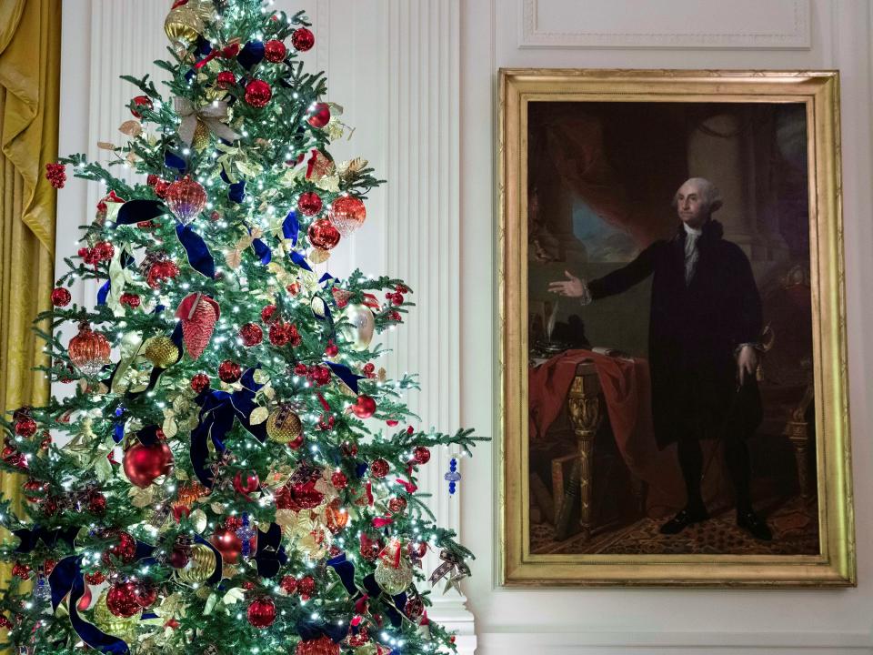 A decorated tree stands next to the portrait of President George Washington in the East Room.