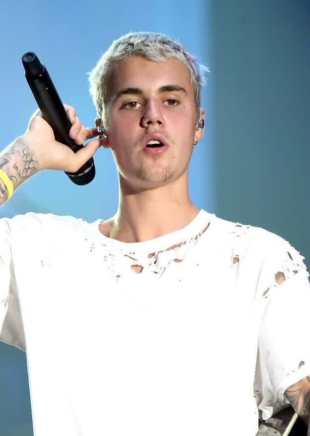 Justin Bieber singing on stage, holding a microphone, wearing a casual torn white shirt