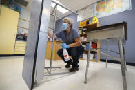 Des Moines Public Schools custodian Cynthia Adams cleans a desk in a classroom at Brubaker Elementary School, Wednesday, July 8, 2020, in Des Moines, Iowa. The cost of bringing students back to classrooms is proving a major stumbling block to safely reopening schools across the U.S. States are furloughing workers, borrowing billions, delaying construction projects and reducing aid to local governments and schools as ways to cope in response to revenue drops that are expected to top 20% in some states, amid the coronavirus pandemic. (AP Photo/Charlie Neibergall)