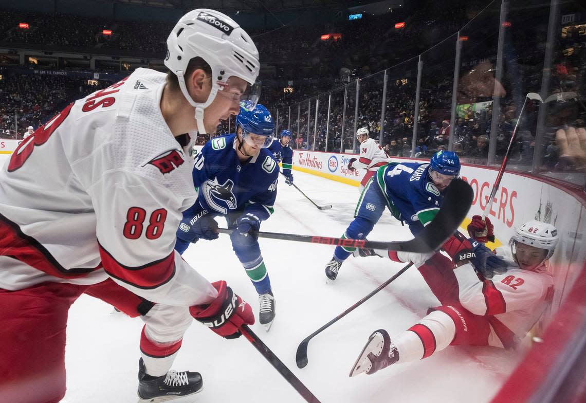 Carolina Hurricanes’ Martin Necas (88), of the Czech Republic, and Jesperi Kotkaniemi (82), of Finland, vie for the puck against Vancouver Canucks’ Kyle Burroughs (44) and Elias Pettersson (40), of Sweden, during the first period of an NHL hockey game in Vancouver, British Columbia, Sunday, Dec. 12, 2021. (Darryl Dyck/The Canadian Press via AP)