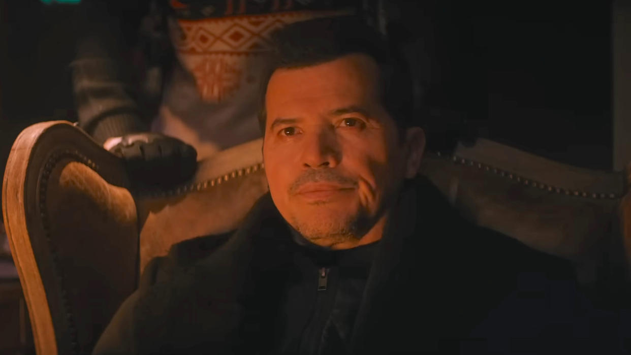  John Leguizamo sitting down in a dimly lit room in Violent Night . 