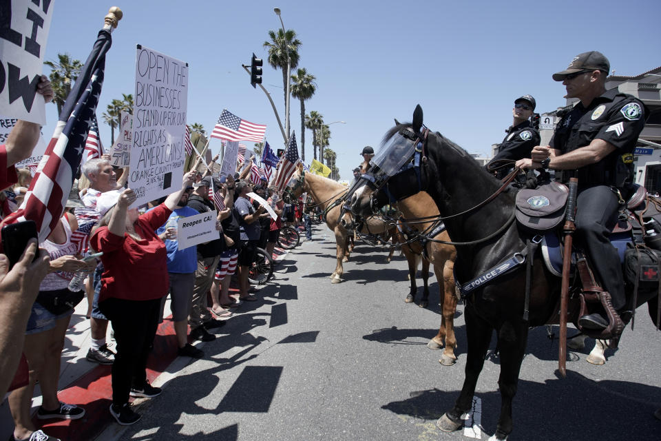 Law-enforcement personnel on horseback keep protesters on the sidewalk during a demonstration on May Day at the pier during the coronavirus pandemic Friday, May 1, 2020, in Huntington Beach, Calif. (AP Photo/Chris Carlson)