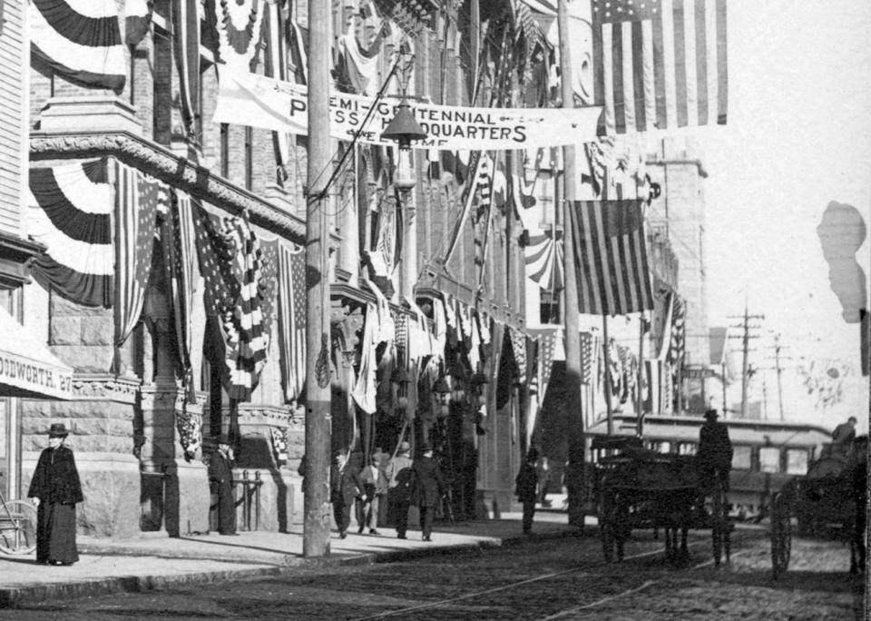 The Five Cent Savings Bank on Purchase Street and signs reading Louis E. Shurtleff, Jeweler, Frank M. Jenkins, Optician, Eyes Tested Free, The Paris, Confectionary-Ice Cream Soda and Charles E. Woodworth, Spectacles, Eye Glasses are situated at New Bedford's Semi-Centennial press headquarters.