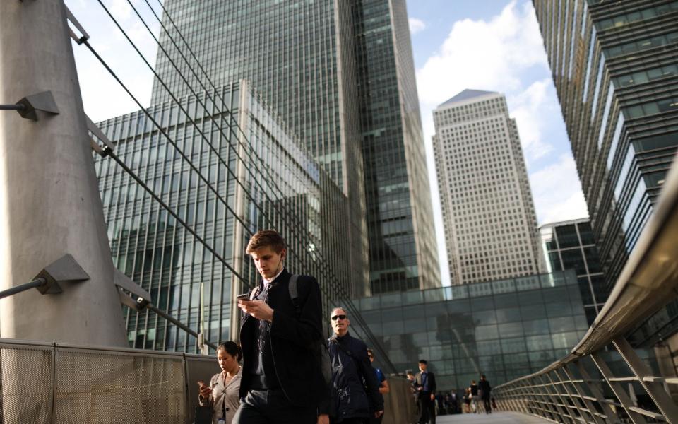 A pedestrian looks at a mobile device as he crosses a raised walkway at the Canary Wharf financial, shopping and business district in London - Simon Dawson /Bloomberg News 