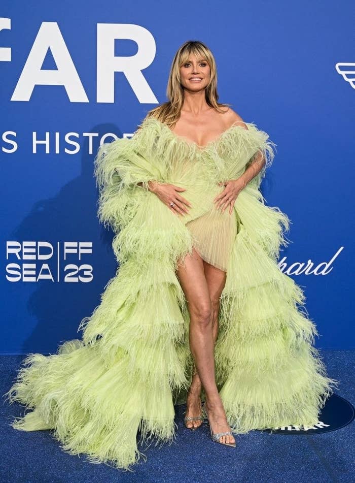 Heidi is wearing a voluminous hi-lo feathered dress that sits off the shoulders