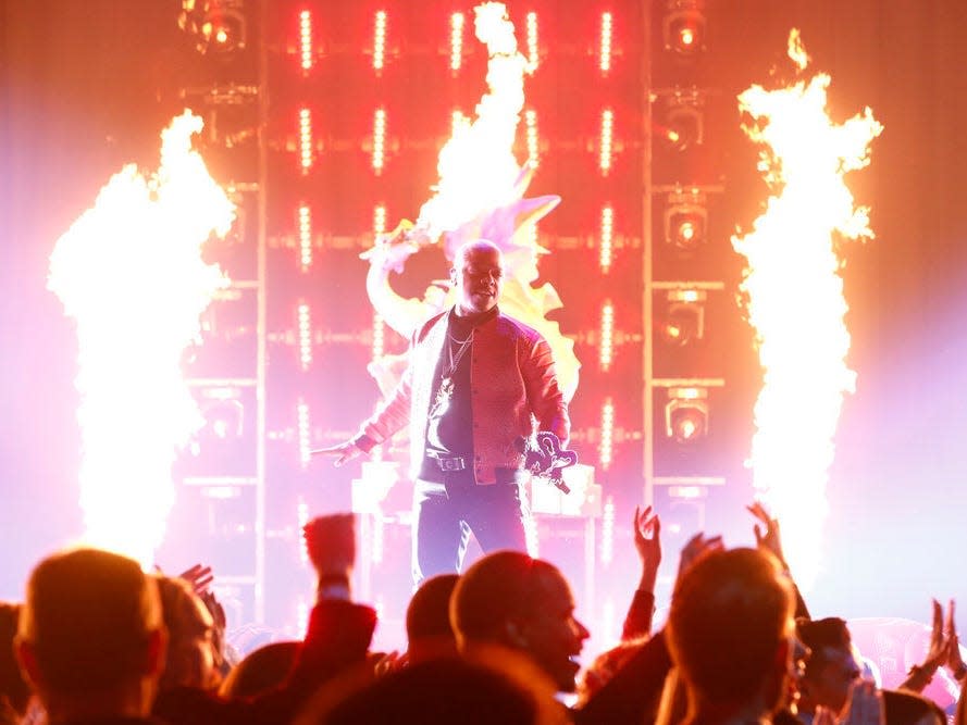 sisqo performing onstage at american song contest, backlit by flames rising from the stage